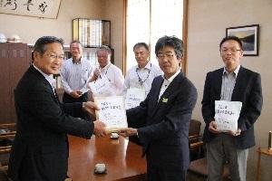 紺色のスーツを着た男性が義援金の入った封筒を関係者の男性に手渡ししている写真