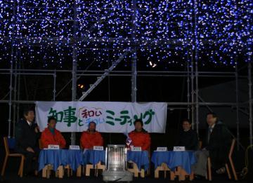 夜、暗くなった会場が青い光のイルミネーションで彩られ、「知事と和い和いミーティング」と書かれた横断幕の前にテーブルが設置され、マイクを持った町長、赤いジャンパーを着たNPO丹波みらい研究会の皆さん、知事が座って意見交換をしている写真