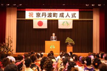 「祝 京丹波町 成人式」と書かれた横断幕のある舞台の演台に立って、寺尾町長が式辞を述べている写真