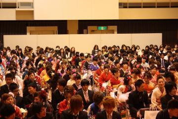 会場いっぱいに振袖を着た新成人やスーツ姿の新成人が座っている成人式の出席者の様子の写真