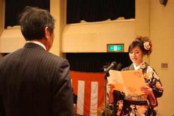舞台で、スーツ姿の男性と向かい合い、スタンドマイクの前に立って、新成人を代表して誓いの言葉を述べている振袖姿の渕上さんの写真
