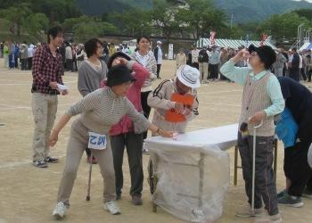 机の上に置かれた健康飲料を手に持ち、参加者が急いで飲んでいる競技中の写真
