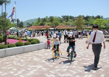 公園内を2台の自転車が横に繋がっている乗り物に乗って、ペダルをこいでいる2人の女の子の写真
