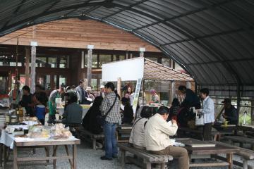 屋外にも色々なブースがあり、椅子と机の設置された場所で来場者の方々が飲食を楽しんでいるなど祭りでにぎわう園内の様子の写真