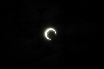 暗闇の中で太陽と月が重なり、月が太陽を隠しきれず、三日月のような形の光の輪が見えている部分日食の写真