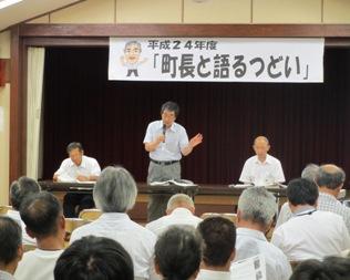 「町長と語るつどい」と書かれた横断幕の前で町長がマイクを持って話をしており、沢山の参加者の皆さんが話を聞いている様子を後方から写した写真