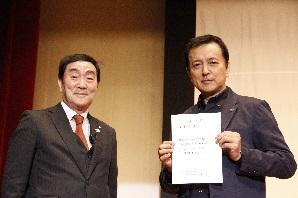 委嘱状を持った映画俳優の榎木孝明さんと町長が並んで写っている写真
