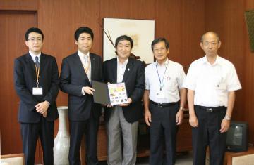 大田喜久夫局長と寺尾豊爾町長が記念切手を持ち、関係者の方々5名が並んで写っている写真