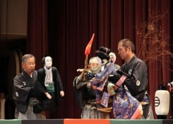 紋付の着物と袴を着た男性が男の人形を操り、右側の男性は着物を着た女の人形を操って「和知人形浄瑠璃」を披露している「和知民芸の集い」の写真