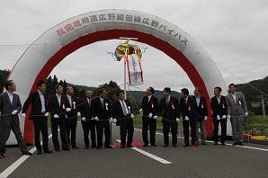 半円型 エアーアーチ門に参列者が横一列に整列しており、門の中央に設置されたくす玉が割れて、参加者が割れたくす玉を見上げている完成祝賀式の様子の写真