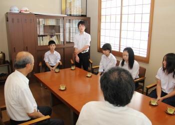 中学生6人と町長、関係者が向かい合って座っており、左奥にいる山鳥勇人さんが席から立って、感想を述べている写真