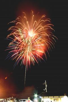 夜空に打ち上げられた、赤や黄色、緑、オレンジなど色鮮やかな花火とオレンジ色の花火が2発綺麗いに上がっている写真