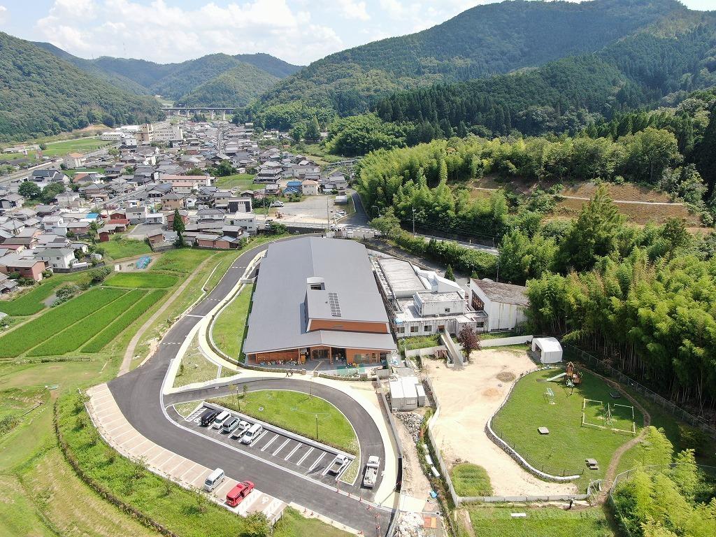 令和3年7月29日の工事進捗、北から撮影した写真。駐車場が完成しており、新しい園舎の横に旧園舎が並んでいる写真。
