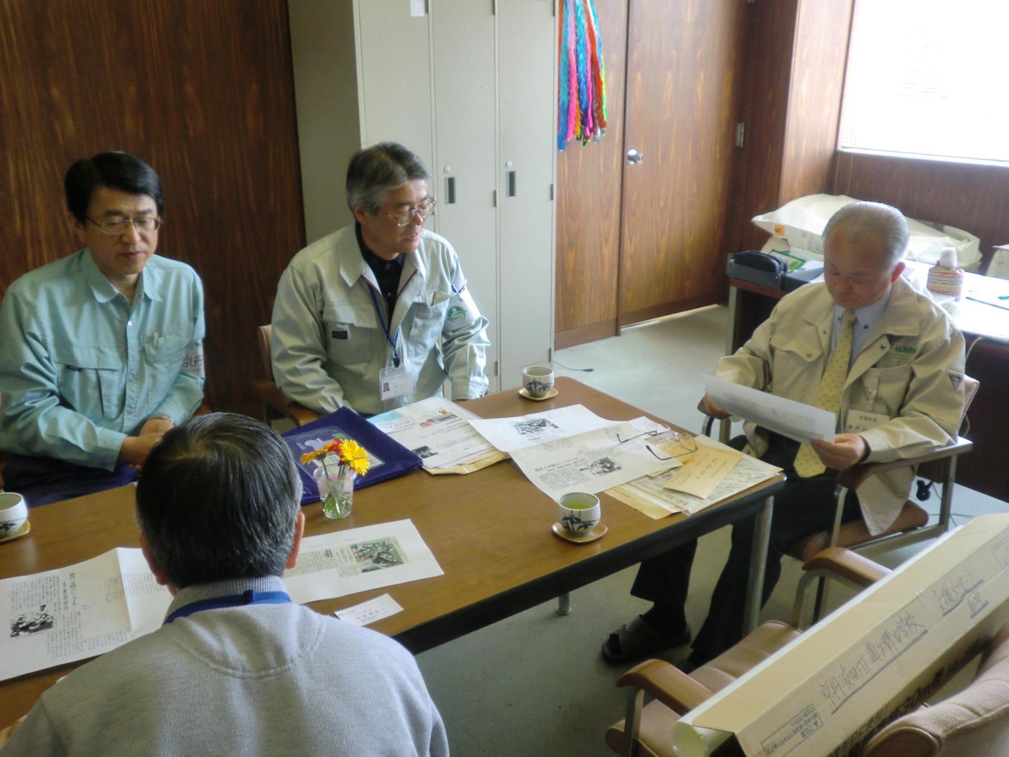資料が置かれたテーブルを囲み話を聞いている調査団員3名と資料を見ながら話をしている町長の写真