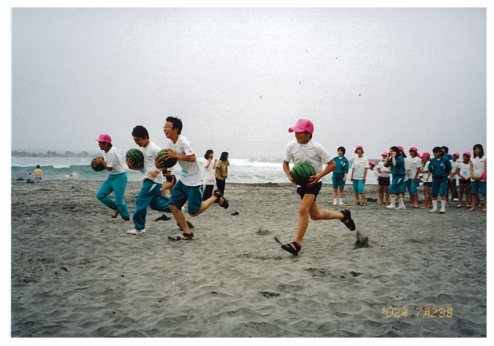スイカを持った子供たち4人が砂浜を競争して走っているスイカ運び競走の様子の写真