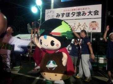みずほ夕涼み大会の看板の前で京丹波町マスコットキャラクター味夢くんと一緒に瑞穂音頭を踊っている参加者の写真
