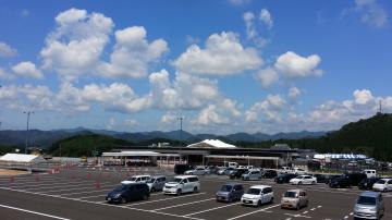 青空の下、遠くには山々が連なり、広々としたアスファルトの駐車場に車が並んでいる写真