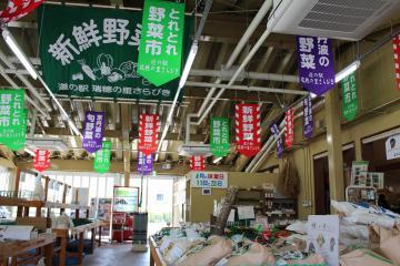 「とれとれ野菜」、「丹波の野菜」「新鮮野菜」などと書かれた緑、紫、赤色の垂れ幕が天井に飾られている店内の写真