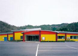 壁の上部が赤、壁の全体が黄色の外壁で建物の前に広い駐車場のある京都・丹波食彩の工房の外観写真