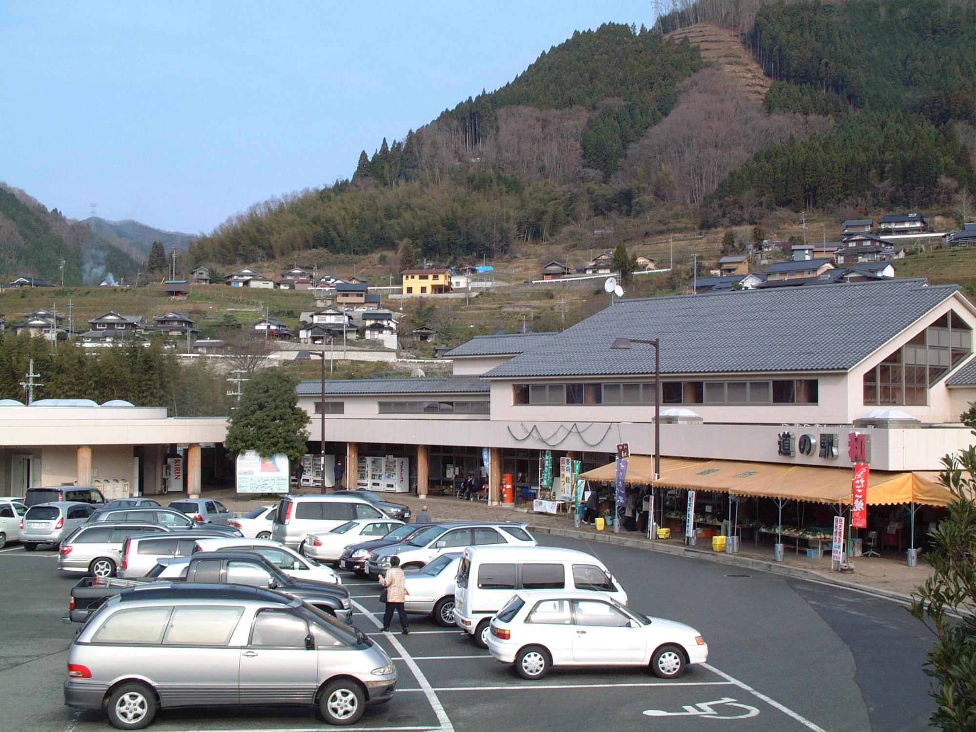 クリーム色の外壁で2階建ての建物と広々とした駐車場、のぼり旗がたっている道の駅和みの外観と店の前の駐車場に停まっている沢山の車の写真