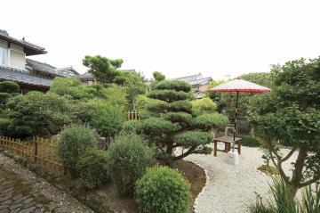 日本庭園のように沢山の木が植えられ、奥に赤い傘の立っている癒庭泉の外観写真