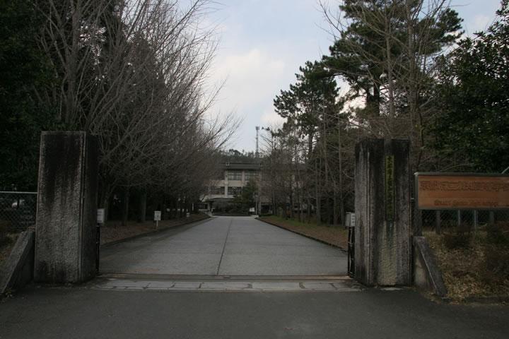 両側に長方形の石の門があり、門から中に入ると奥に見える校舎まで続く歩道の両側に木々が植えらている須知高等学校の外観写真