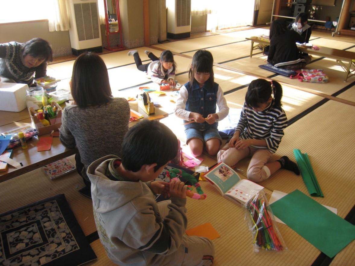 畳の部屋で子ども達が折り紙や画用紙を使って工作をしているふれあいサタデークラブの活動の様子の写真