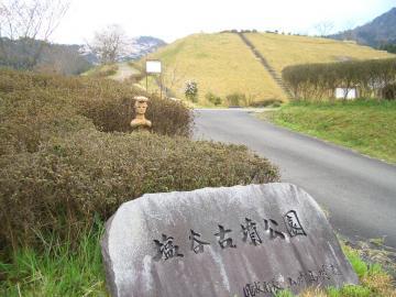 入り口に「塩谷古墳公園」と書かれた石碑と、その後ろの植え込みの間に埴輪が見えている写真