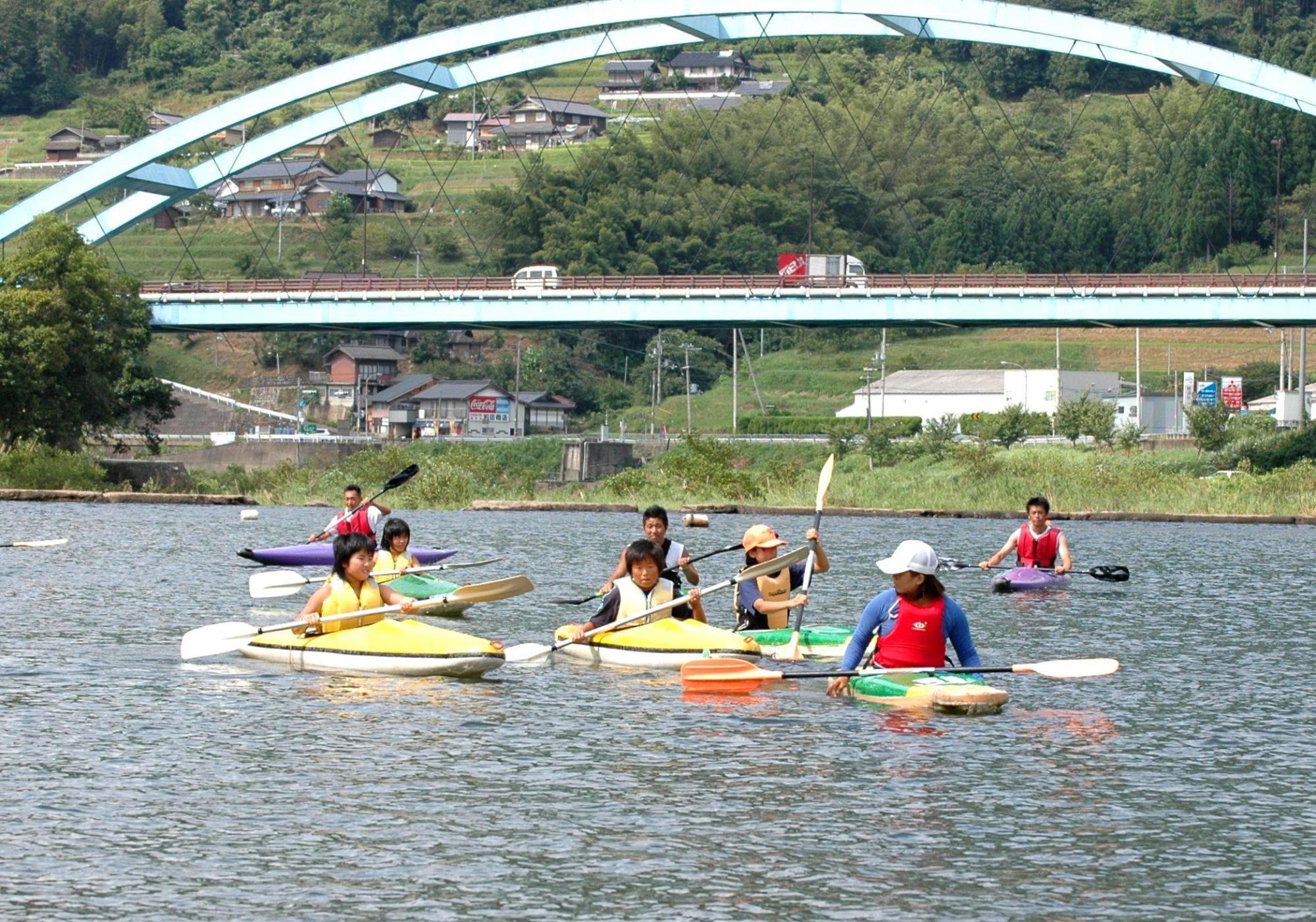 由良川で指導員の指導を受けながらカヌーに乗りオールを漕いでいる参加者たちの写真