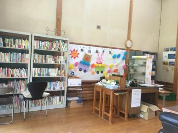壁にウサギとクマが電車に乗っている壁面飾りがあり、壁側に本が沢山並んだ本棚、本棚の前に椅子が並んでいる梅田公民館図書室内の写真
