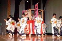 室内で高台の周りで着物を着た女性たちが踊っている和知文七踊りの様子の写真
