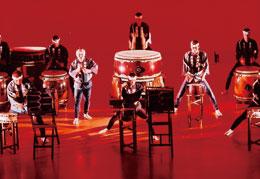 赤色の背景と照明の中、笛や大小様々な種類の太鼓を叩いて演奏している丹波八坂太鼓の写真