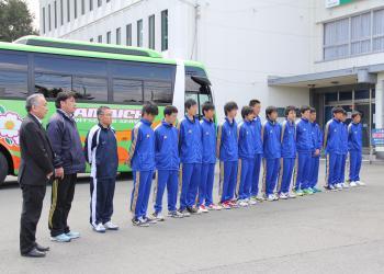 大型バスの前に、青いジャージを着た須知高校ホッケー部の部員と関係者が横一列に整列して激励を受けている写真