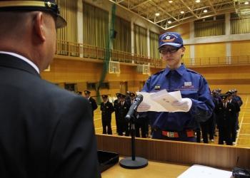 消防の活動服を着た新入団員が演台の前に立ち、手に式辞用紙を持って誓いを述べている写真
