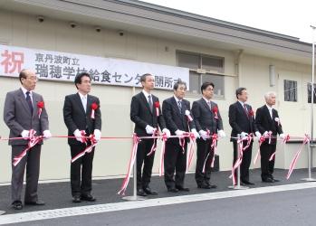 「祝 京丹波町立 瑞穂学校給食センター開所式」と書かれた横断幕の前に紅白のテープカットが準備され、寺尾町と関係者の方々がハサミを持って、テープカットをしようとしている写真