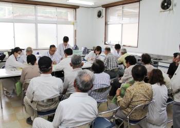 前方の長机に医療従事者の方々が座っており、問診を受けるために、たくさんの住民がパイプ椅子に座って順番待ちをしている写真