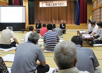 「町長と語るつどい」と書かれた横断幕が前方に掲げられ、横断幕の前の長机に座っている関係者、向かい合うように多くの参加者が座布団に座り、話を聞いている写真
