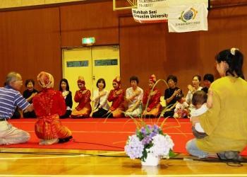 踊りの衣装を着たインドネシアからの訪問団と来場者が交互に並んで大きな輪を作って座り、交流が行われている写真