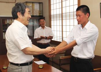 寺尾町長とキャプテンの原澤君が両手を握って握手しており、町長が笑顔で激励している写真