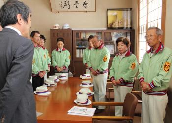 薄いグリーンのユニフォームを着た選手の方々が寺尾町長と向かい合って話をしている写真
