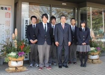 ハボタンや南天で飾られた門松が玄関前に設置され、役場を訪れた須知高校の学生5名と寺尾町長が門松の間に並んで写っている記念写真