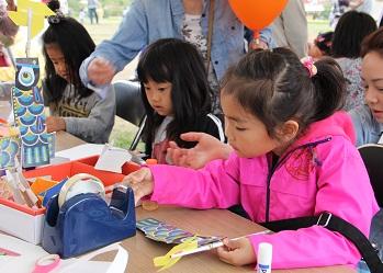 女の子たちがテーブルの前に座り、セロハンテープを使って、こいのぼりを作る作業に真剣な表情で取り組んでいる写真