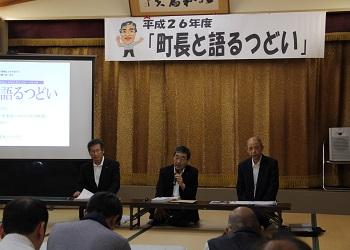 「町長と語るつどい」と書かれた横断幕の前に長机が置かれ、3名の関係者が参加者の前に座っており、中央に座っている町長がマイクを持って話をしている写真