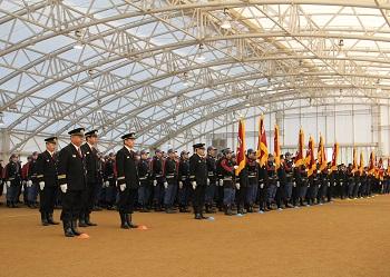 消防団の半纏を着た消防団員が団ごとに旗を持って整列しており、消防団の制帽、制服を着た関係者も直立して立っている出発式の写真