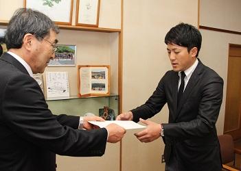 寺尾町長から辞令を両手で受け取る黒いスーツ姿の小松さんの写真