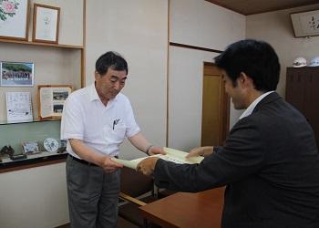 グレーのスーツを着た関係者の男性が寺尾町長に感謝状を手渡している写真