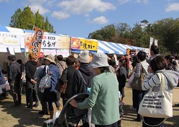 唐揚げ、焼きカレーなどの色々な食べ物の屋台が並んでおり、たくさんの人の行列が屋台の前に出来ている写真