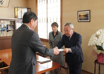 紺色のスーツ姿の中西会長が寺尾町長に答申書を手渡ししており、中西会長の横に立つ関係者の女性が一緒に頭を下げている写真