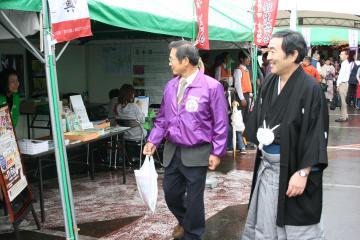 紋付き袴姿の寺尾町長と紫色のジャンパーを着た副町長が笑顔でテントの立ち並ぶ会場内の様子を見て回っている写真