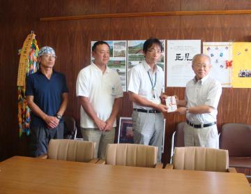 名札を首にかけている派遣団の男性が井戸川町長に支援金を手渡しており、他2名の関係者の男性と並んで写っている写真